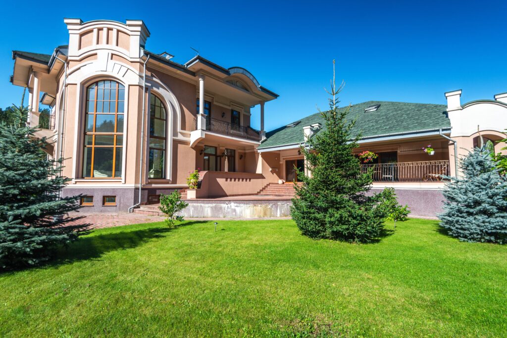 Modern luxury villa with large windows, surrounded by lush green lawn and trees.
